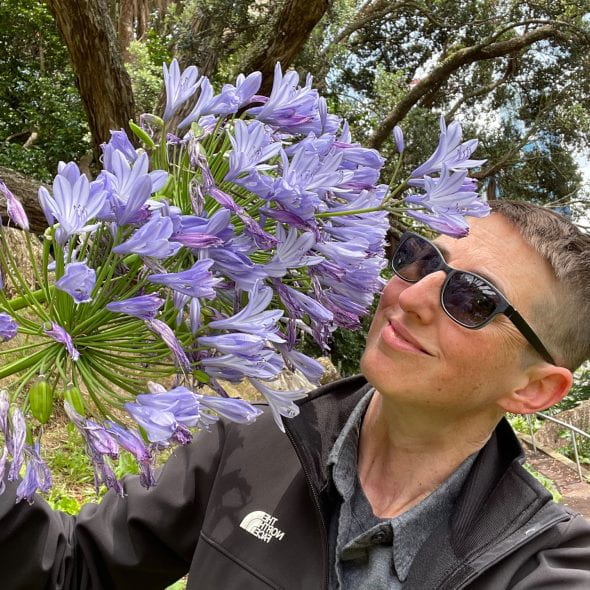 person with sunglasses posing with large flowers